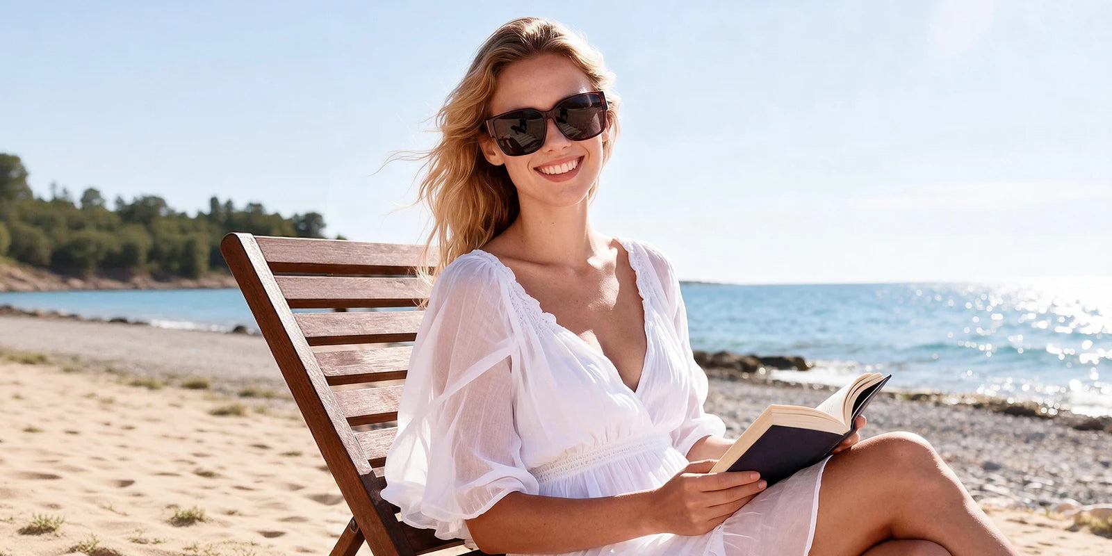 Woman wearing sunglasses while reading by the sea